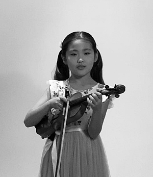 A young girl stands with her violin in her hand.