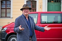 A man in a hat stands in front of a red bus, holding a key in his hand