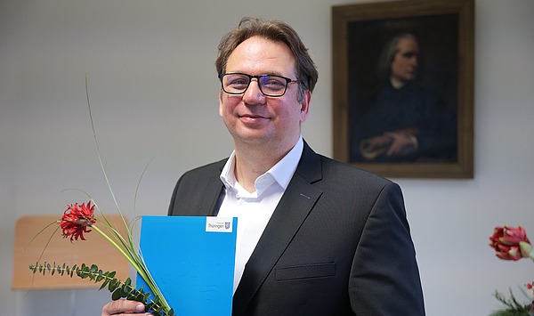Das Bild zeigt einen Mann mit einer Urkunde und einer Blume.