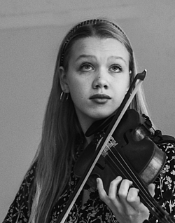 A young girl stands with her violin and looks up. 