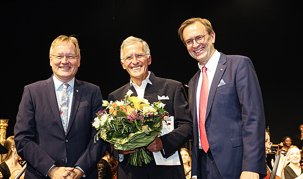 Das Bild zeigt drei Personen und einen Blumenstrauß.