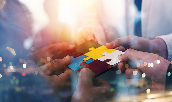 The picture shows hands assembling a puzzle in the air. Das Bild zeigt Hände, die in der Luft ein Puzzle zusammensetzen.