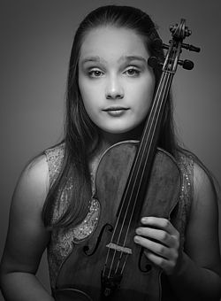 Young girl stands with her violin and looks into the photo.
