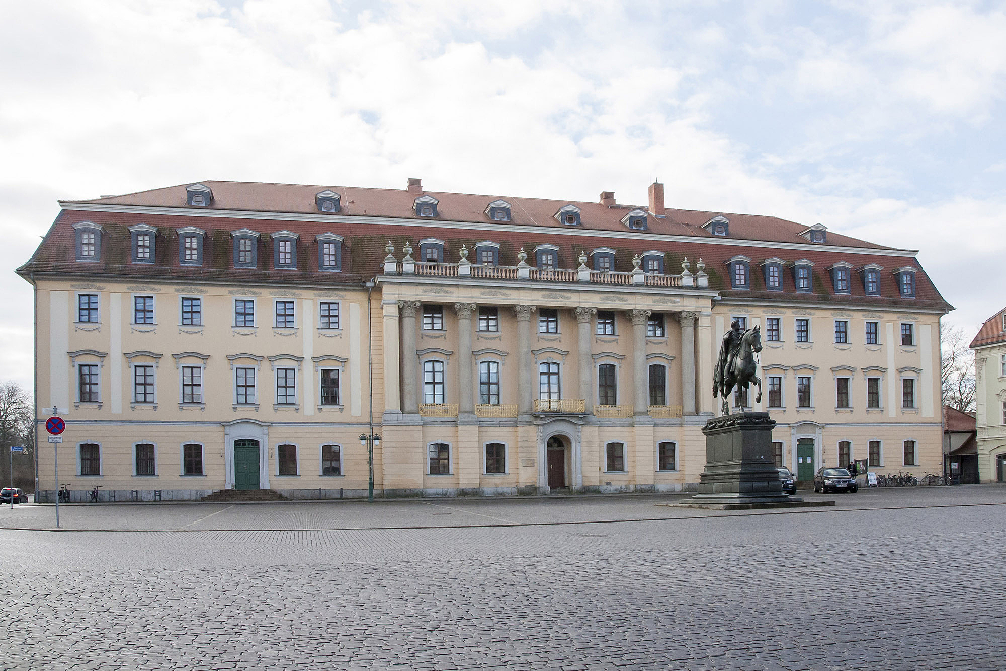 Das Bild zeigt ein großes Gebäude mit Säulen auf einem Platz.