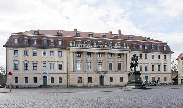 Das Bild zeigt ein großes Gebäude mit Säulen auf einem Platz.