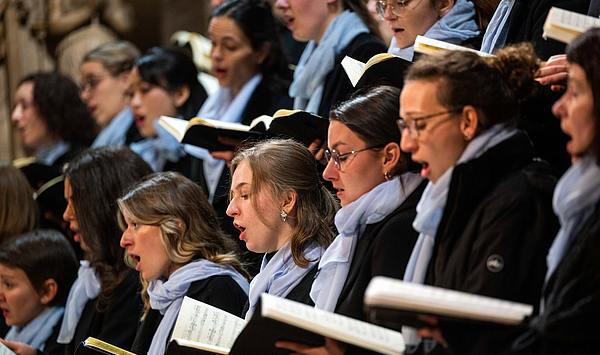 Das Bild zeigt Menschen, die Noten halten und singen. 