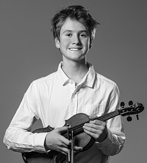 Ein Junge steht mit seiner Violine in der Hand und lächelt in das Foto.