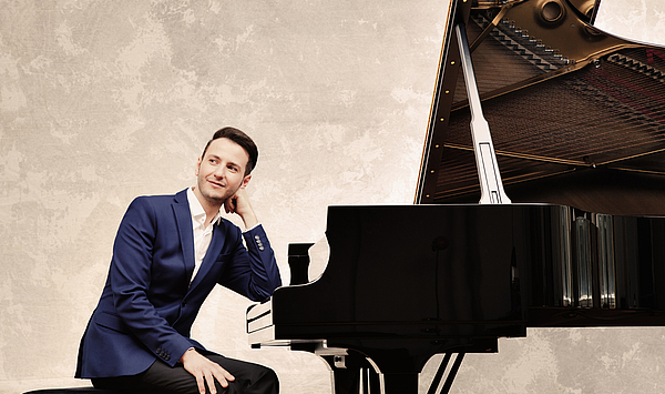The picture shows a man in front of a grand piano. Das Bild zeigt einen Mann vor einem Konzertflügel.