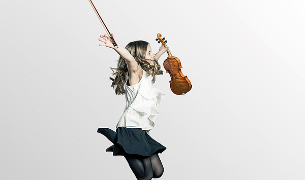 Auf dem Bild ist eine in die Luft springende junge Geigerin zu sehen, die die Geige und den Bogen hochhält. 
