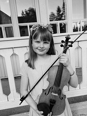 Ein junges Mädchen mit Violine steht auf einer Veranda. 
