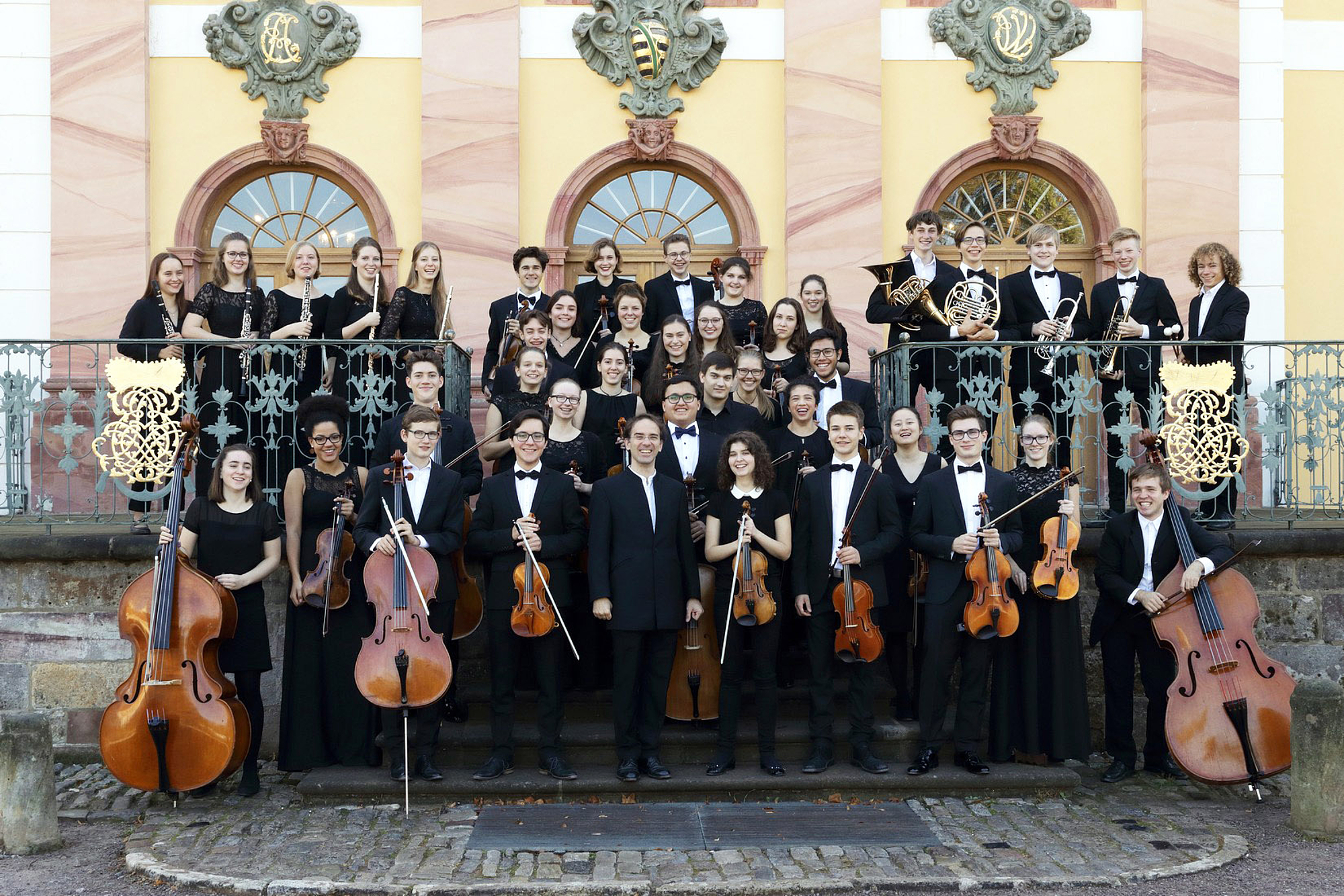 The picture shows a group of people in front of a castle façade. Das Bild zeigt eine Gruppe von Menschen vor einer Schlossfassade.