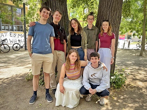 Das Bild zeigt eine Gruppe von jungen Menschen vor zwei Bäumen