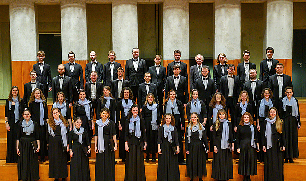 Singers of the chamber choir stand lined up in concert dress. They look into the camera. Sänger und Sängerinnen des Kammerchors stehen aufgereiht in Konzertkleidung. Sie schauen in die Kamera.