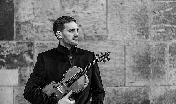 The picture shows a man with a viola in his arms. Das Bild zeigt einen Mann mit einer Bratsche im Arm.