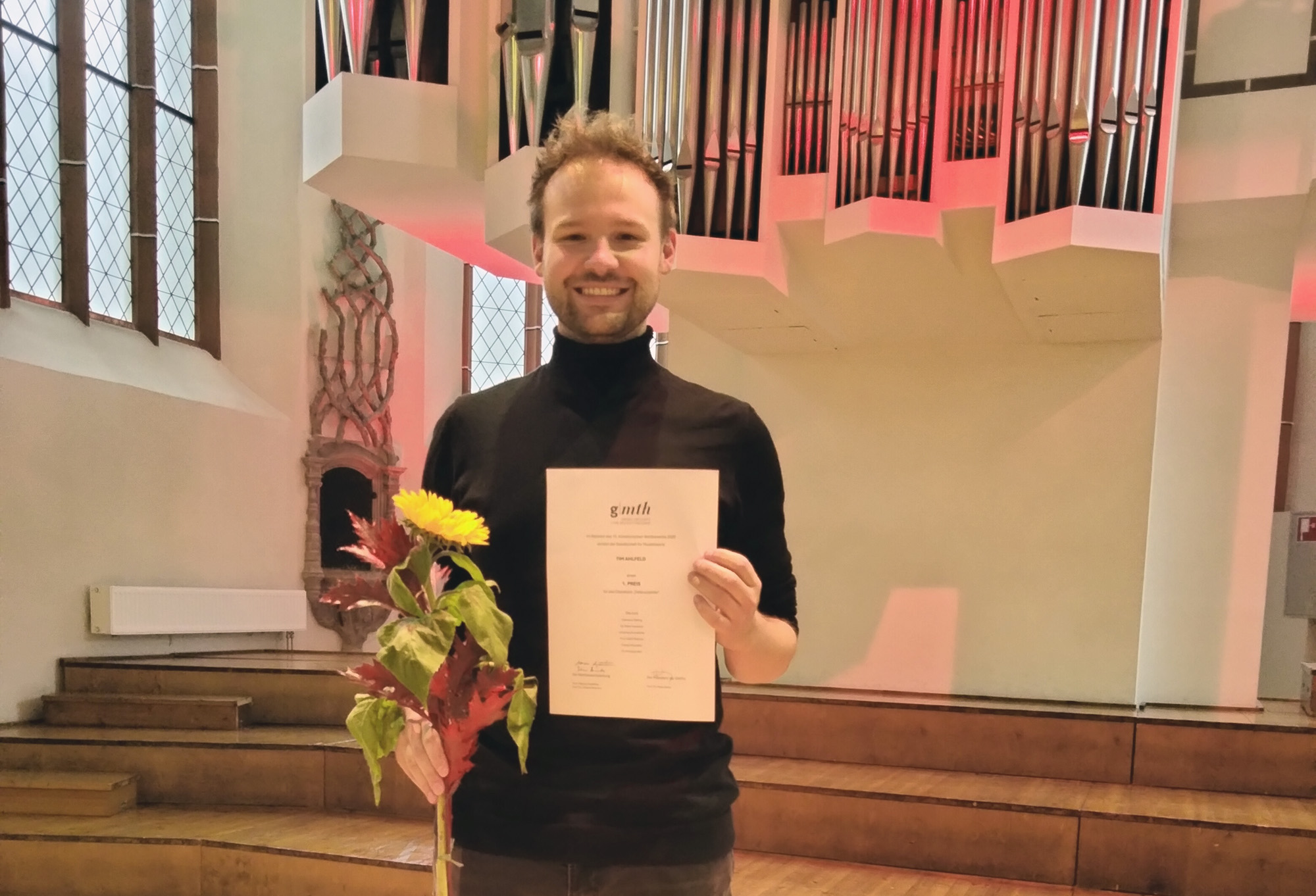 Das Bild zeigt eine Person mit Blumenstrauß und Urkunde.