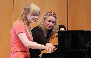 The picture shows a piano student and a teacher at the concert grand piano.