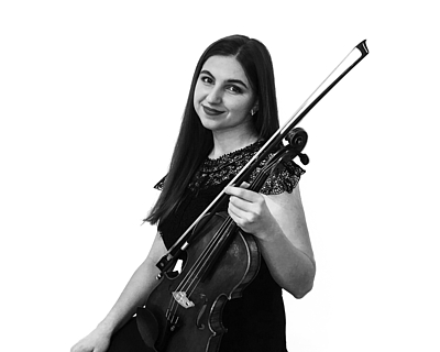 Young girl stands with her violin and looks into the photo.