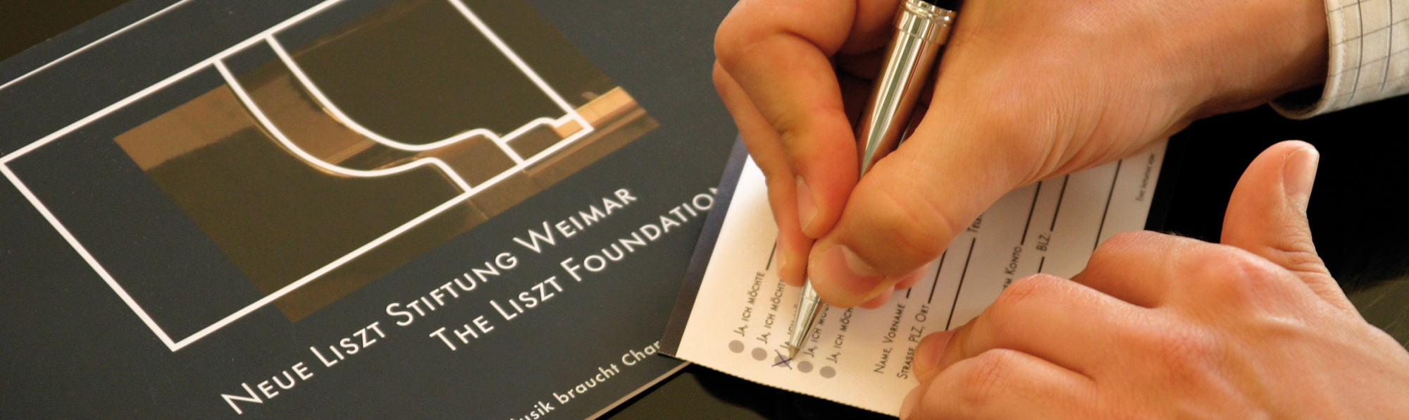 The picture shows a hand with a pen on a form.