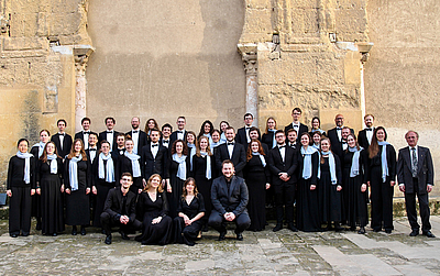 The picture shows a choir in front of a wall.