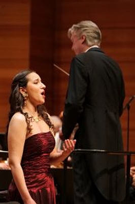 The picture shows a woman singing and a conductor.
