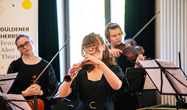 Das Bild zeigt Musiker mit einer Flöte und Streichinstrumenten.