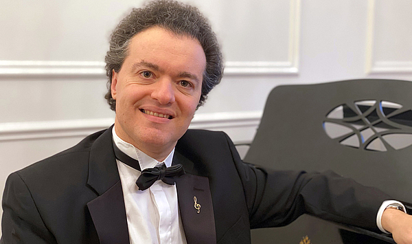 Das Foto zeigt einen Mann mit dunklen Haaren, der an einem Klavier sitzt. Das Foto zeigt einen Mann mit dunklen Haaren, der an einem Klavier sitzt.