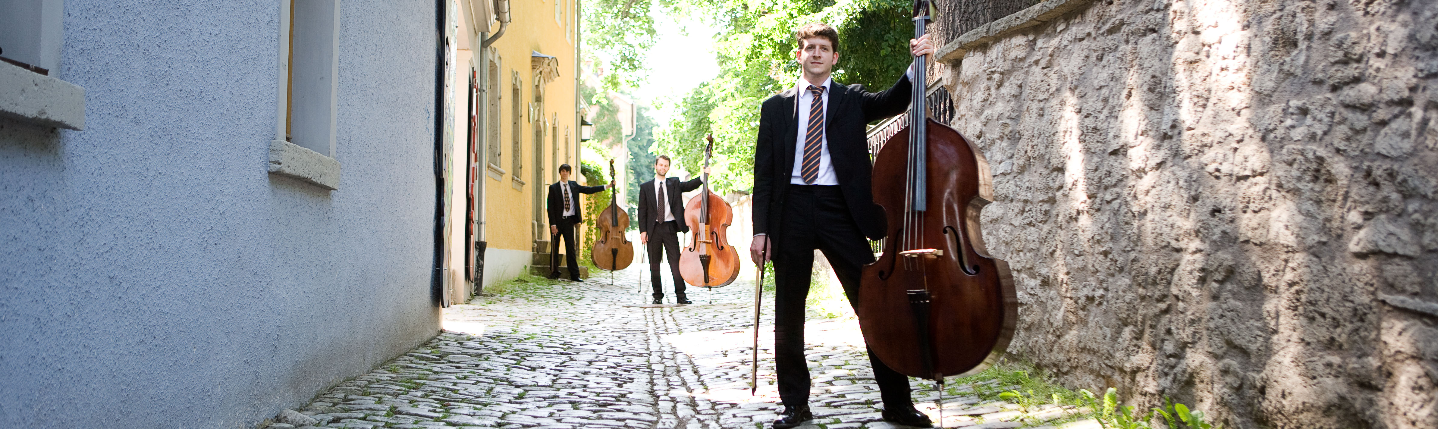 Das Bild zeigt Personen mit Instrumenten in einer Gasse.