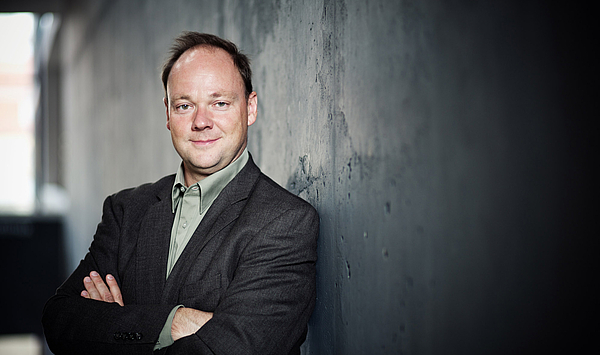 The picture shows a man with dark hair and arms folded on his chest. Das Bild zeigt einen Mann mit dunklen Haaren und auf der Brust verschränkten Armen.