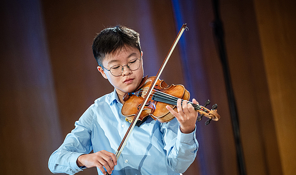 A young man with dark hair plays on a violin. Ein junger Mann mit dunklen Haaren spielt auf einer Geige.