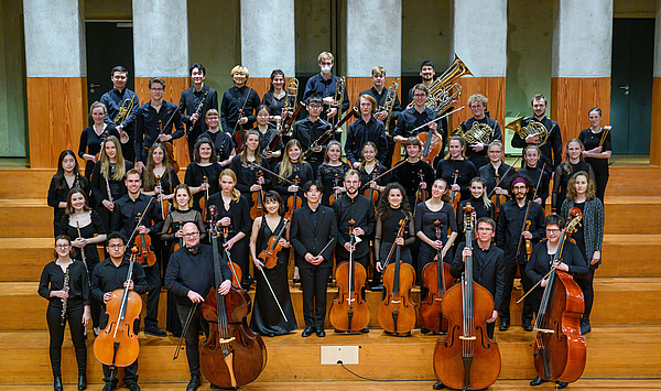 Das Bild zeigt ein Orchester auf Treppenstufen. 