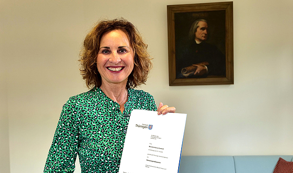 Das Bild zeigt eine Frau mit einer Urkunde.