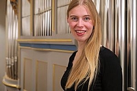 Eine junge Frau mit blonden Haaren steht vor Orgelpfeifen