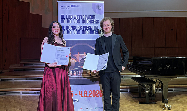 Das Bild zeigt zwei Personen mit Urkunden.